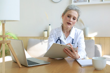 年长的女医生治疗师戴着耳机进行视频通话，通过视频电话聊天与网络摄像头在线咨询虚拟患者。