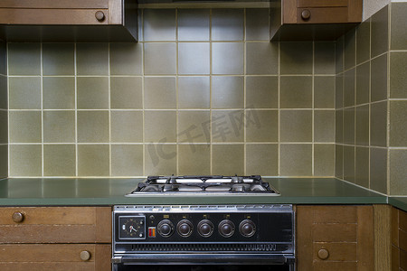 旧式复古厨房的内部配有带棕色木柜的古董烤箱、绿色的旧学校时尚瓷砖，需要翻新
