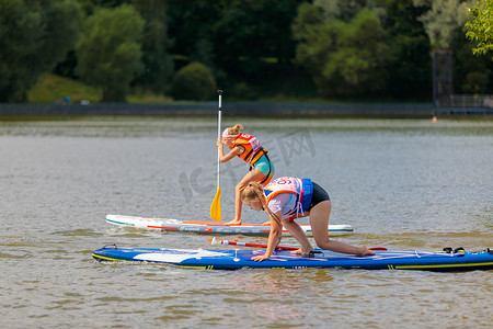 划水摄影照片_一个孩子在冲浪板上游泳，用桨划水。