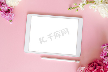 带白色屏幕的 iPad pro 平板电脑，粉红色背景，带笔和鲜花。