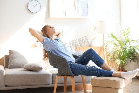 家里的年轻女人坐在窗前的现代椅子上，在客厅里放松。