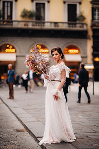 美丽的花朵图案摄影照片_佛罗伦萨的新娘带着美丽的花朵图案作为面具，时尚的新娘穿着婚纱带着面具站在佛罗伦萨的老城区。