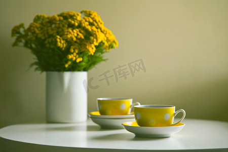 复古茶具-白色桌子上的两个黄色点缀复古杯子和黄色菊花。