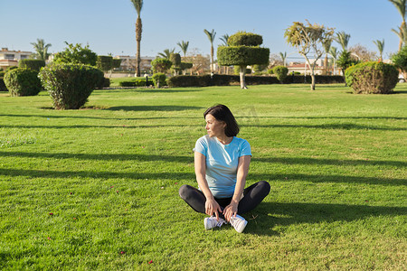 阳光明媚的夏日早晨，中年女性进行户外运动，40 多岁的女性坐在草地上