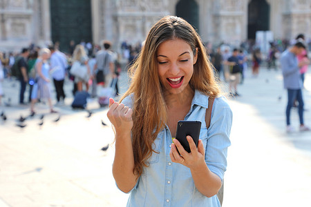 手机批准摄影照片_兴奋的年轻女子在街上用智能手机在线收到好消息