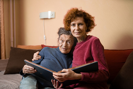 积极的老年女士坐在家里的沙发上看着相册照片，开朗的朋友。