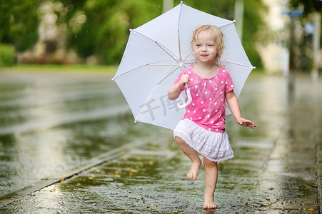 可爱的蹒跚学步的小女孩在雨中玩得开心