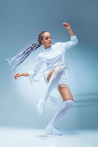 嘻哈女摄影照片_穿着运动服的迷人兴奋的健身女舞者在蓝色背景下跳舞。