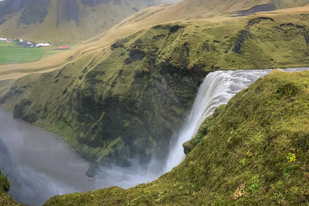 绿色岩石间暴雨期间冰岛瀑布顶部的 Skogafoss 瀑布