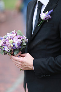 白种人新郎穿着黑色西装和领带保留花束。