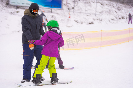 男人滑雪摄影照片_教练在雪坡上教孩子滑雪