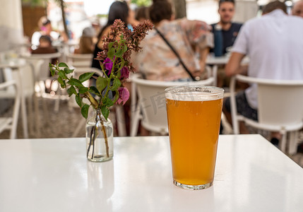 里斯本酒吧或咖啡馆的白桌上放着一品脱凉爽的 IPA，上面放着鲜花