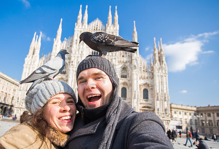 冬季旅行和度假概念 — 快乐的游客在米兰大教堂前与滑稽的鸽子拍自画像
