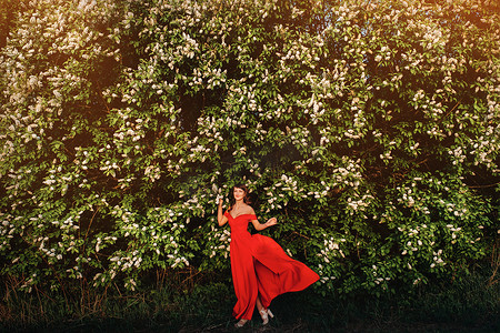 日落时，一个穿着红裙、红唇的女孩站在一棵大白花树旁