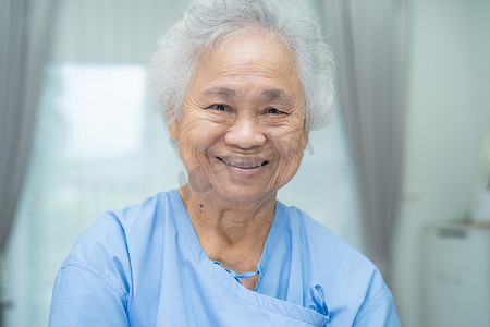亚洲老年或老年老妇女病人坐在护理医院病房的床上，脸上笑容灿烂，健康强大的医疗理念。