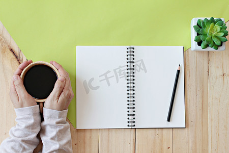 拿着空白笔记本和铅笔的女人拿着热咖啡