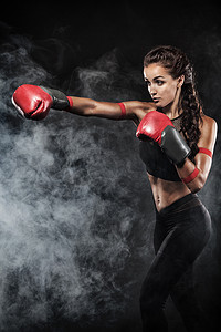 一位运动能力强的女拳击手，在黑色背景下进行拳击训练。