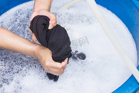女手在盆里用洗涤剂手洗衣服。