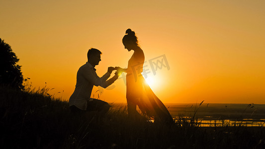 男人跪下向女人高山求婚的浪漫剪影-情侣在日落时订婚-戴上戒指女孩的手指，慢动作