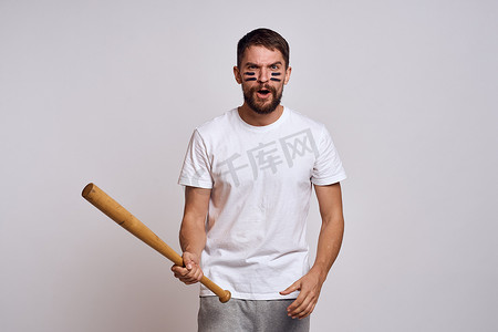 一位情绪激动的男子，穿着白色 T 恤，在浅色背景上拿着棒球棒，他用手向模特做手势