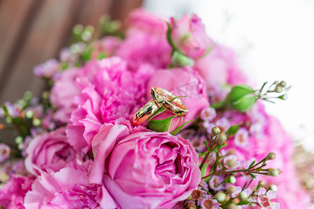 新娘花束上的金色结婚戒指，上面有粉红色和淡紫色的玫瑰。