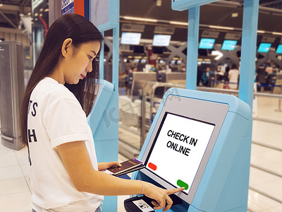 持有护照的年轻亚洲女性在机场使用自助值机亭触摸屏交互式显示屏，在机场航站楼的自动设备上进行航班自助值机或购买机票