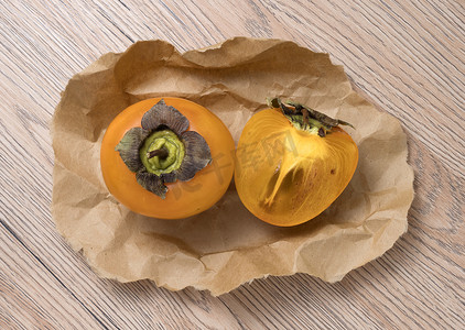 柿子果实摄影照片_木制背景上美味成熟的柿子果实。