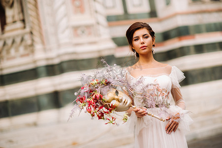 美丽的花朵图案摄影照片_女孩新娘以美丽的花朵图案作为佛罗伦萨的面具，穿着婚纱的时尚新娘戴着面具站在佛罗伦萨老城。