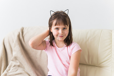 猫耳朵摄影照片_可爱的小女孩，长着猫耳朵，坐在沙发上。