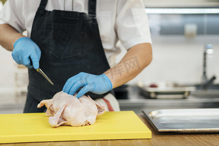 前视图厨师戴着手套切鸡肉。