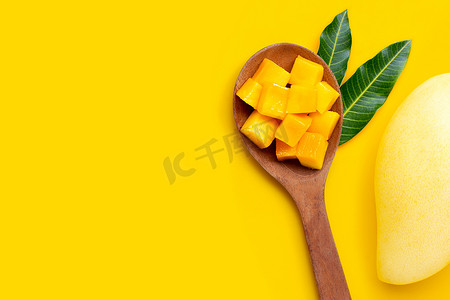 在黄色背景的木勺上切熟的芒果块。