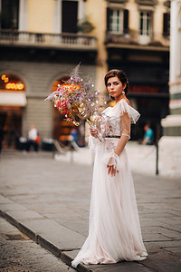 女孩新娘以美丽的花朵图案作为佛罗伦萨的面具，穿着婚纱的时尚新娘戴着面具站在佛罗伦萨老城。