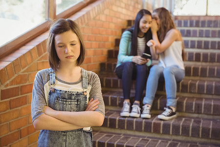 悲伤摄影照片_学校朋友在学校走廊欺负一个悲伤的女孩