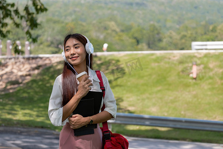 快乐的年轻美丽的亚洲女人戴着耳机，拿着笔记本在公园里。