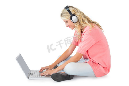 漂亮的年轻金发女郎坐着用笔记本电脑听音乐