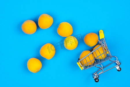 买水果摄影照片_蓝色背景上有杏子的购物篮。购物车