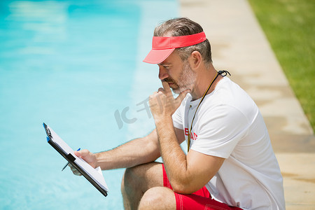 健身游泳教练摄影照片_游泳教练在泳池边看剪贴板