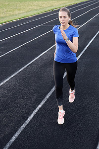 女孩跑道摄影照片_跑步运动员在田径跑道上跑步，在体育场训练她的有氧运动。