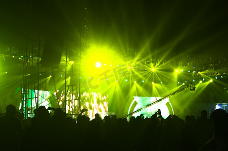 剪影观众人群站在绿色舞台灯前的音乐会表演流行摇滚音乐生活事件颁奖典礼上，享受欢呼举起双手面对乐队。