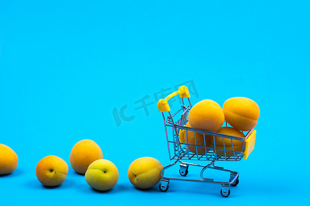 水果商店摄影照片_蓝色背景上有杏子的购物篮。购物车