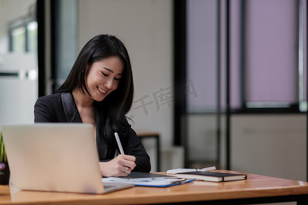 亚洲女性手拿笔，同时使用数字平板电脑进行财务分析