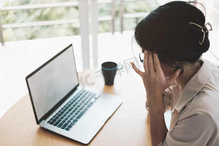 疲惫的亚洲女商人因笔记本电脑工作而头痛，在办公室感到头痛，在工作中感到不舒服