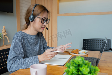 亚洲女性戴耳机看笔记本电脑，享受与导师在线学习、听音频讲座、观看网络研讨会准备考试、电子学习、自学概念