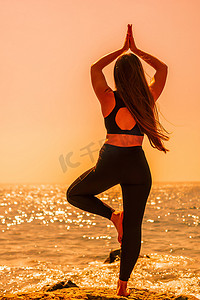 长发的年轻女子，穿着运动服紧身裤和上衣的健身教练，在普拉提前伸展身体，在阳光明媚的日子里在海边的瑜伽垫上，女性健身瑜伽常规概念