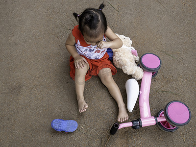 哭泣摄影照片_亚洲小女孩摔倒膝盖受伤后坐在地上。