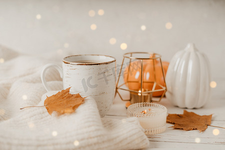 一杯咖啡摄影照片_静物细节、一杯茶或咖啡、南瓜、蜡烛、白桌背景上有叶子的早午餐、舒适房子里的家居装饰。