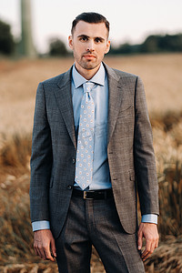 西装和领带摄影照片_麦田里一位身穿灰色西装的商人的肖像。穿着夹克和领带的大自然中的男人