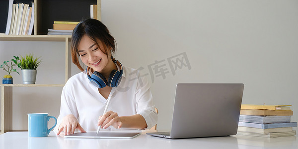 年轻的本科生通过笔记本电脑学习在线课程，并在数字平板电脑上记笔记。