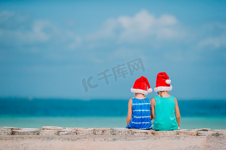 圣诞海滩度假期间戴着圣诞老人帽子的可爱小孩。