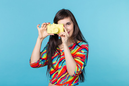 微笑的年轻女子手里拿着一个黄色的老式相机模型，在蓝色背景上摆出姿势，并有复制空间。